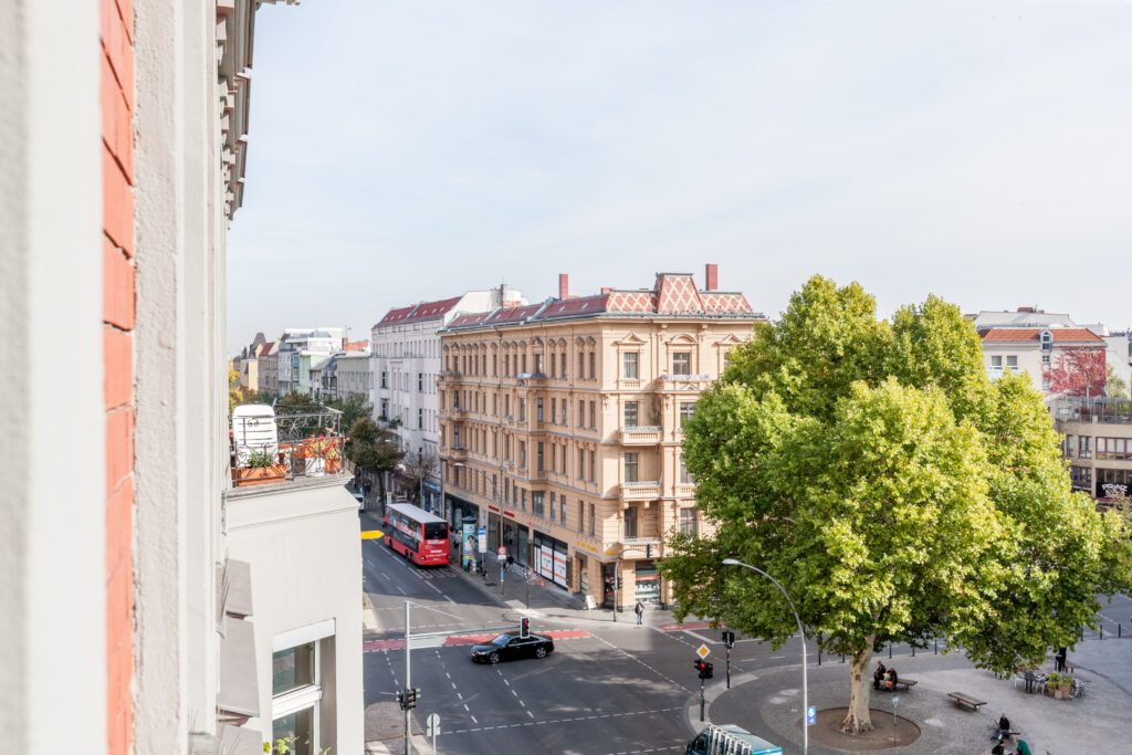 Blick aus dem Fenster auf eine baumgesäumte Straße und Gründerzeitgebäude.