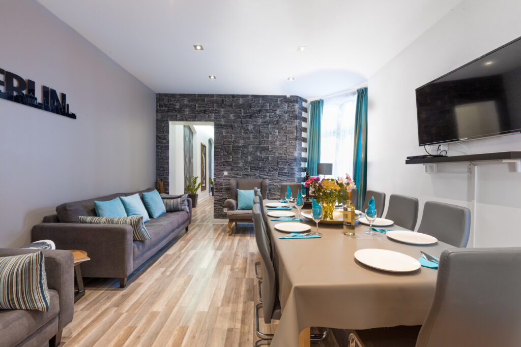 Offener Wohn-Essbereich mit Holztisch, grauer Couch und Fernseher.