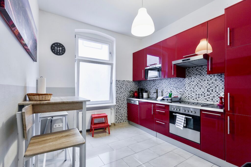 Rote Hochglanzküche mit Holzfußboden und Edelstahlelementen.
